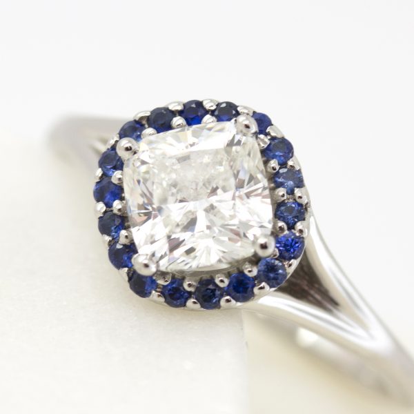 cushion cut centre diamond with blue sapphire halo set on a bias with split shank engagement ring