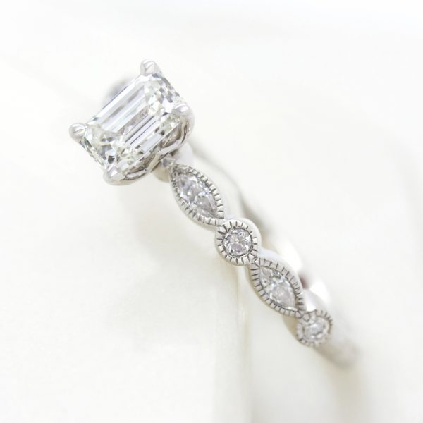 emerald cut diamond engagement ring with marquise and round diamond band and milgrain